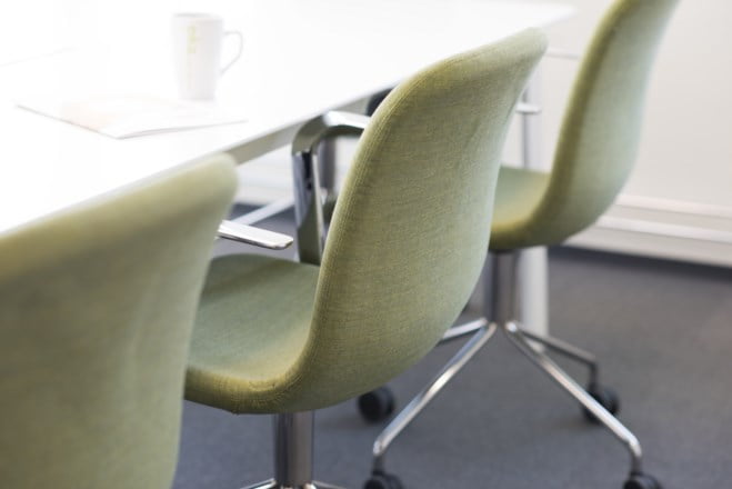 Et møterom med grønn stoler inntil et bord med kaffekopp på